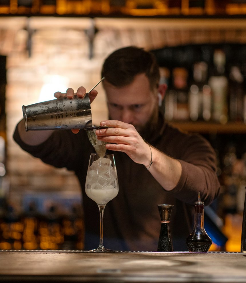 Bartender straining a cocktail during service at a dimly lit bar