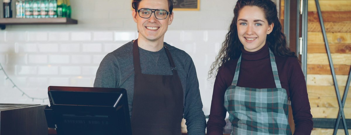 Two coffee shop team members smiling behind the register