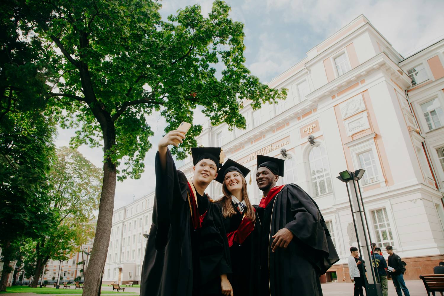 Three graduates in caps and gowns taking a selfie on campus